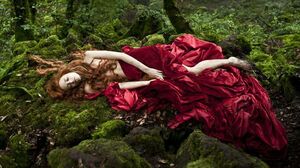 Beautiful woman in red dress lying in the forrest in Tale of